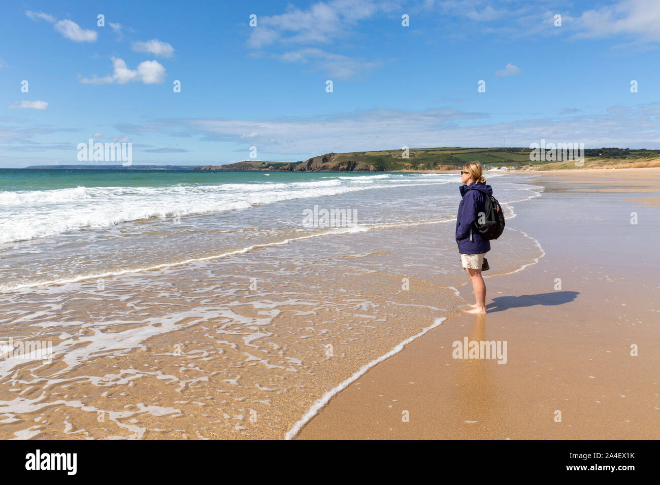 A female walker paddles in the calm surf on the beach at Praa Sands, Cornwall, England, United Kingdom. Stock Photo