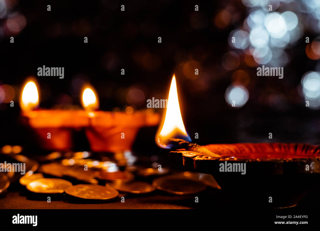 Closeup of earthen terracotta lamps glowing, in Diwali decoration concept with coins on the floor Stock Photo