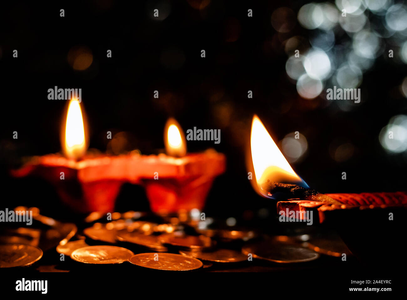 Deepawali concept. Low light Photo of two blurred earthen lamps with one lamp in the foreground and some coins on the floor Stock Photo