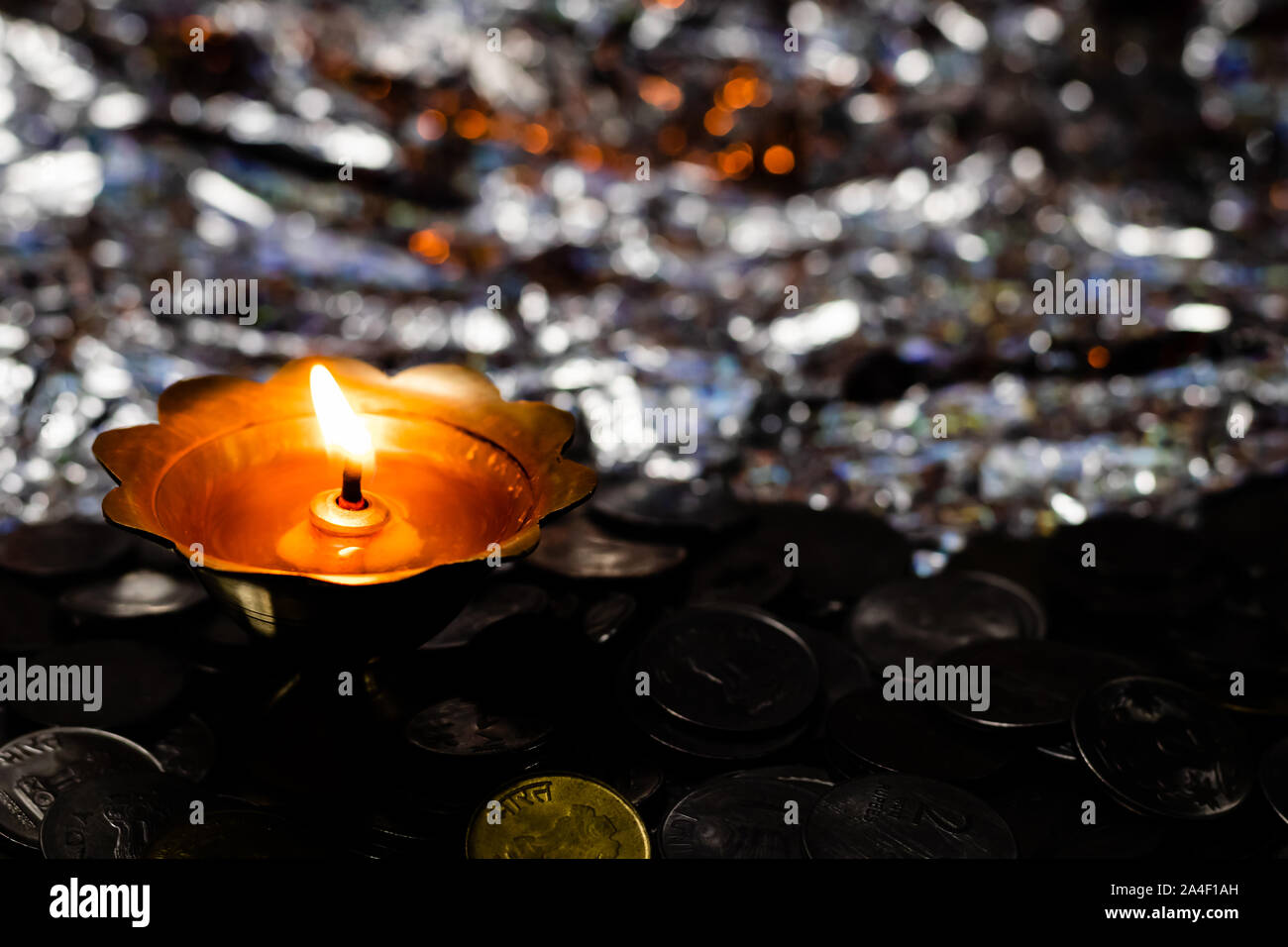 Top view of a glowing metal-lamp on a pile of coins and reflective background. Dhanteras concept Stock Photo