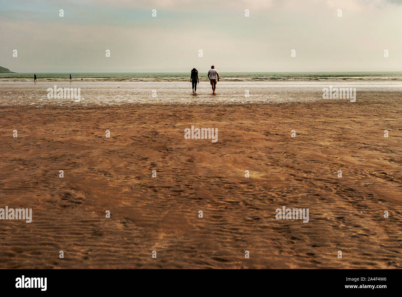 Couple walking on sandy beach leaving footprints in the sand. One ...