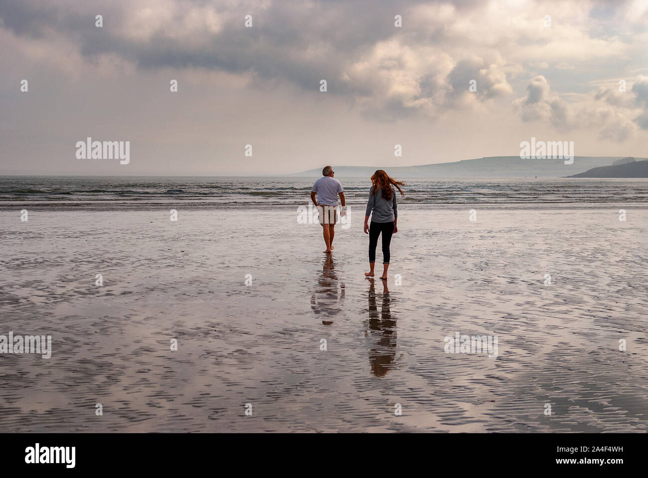 Couple walking on sandy beach leaving footprints in the sand. One ...
