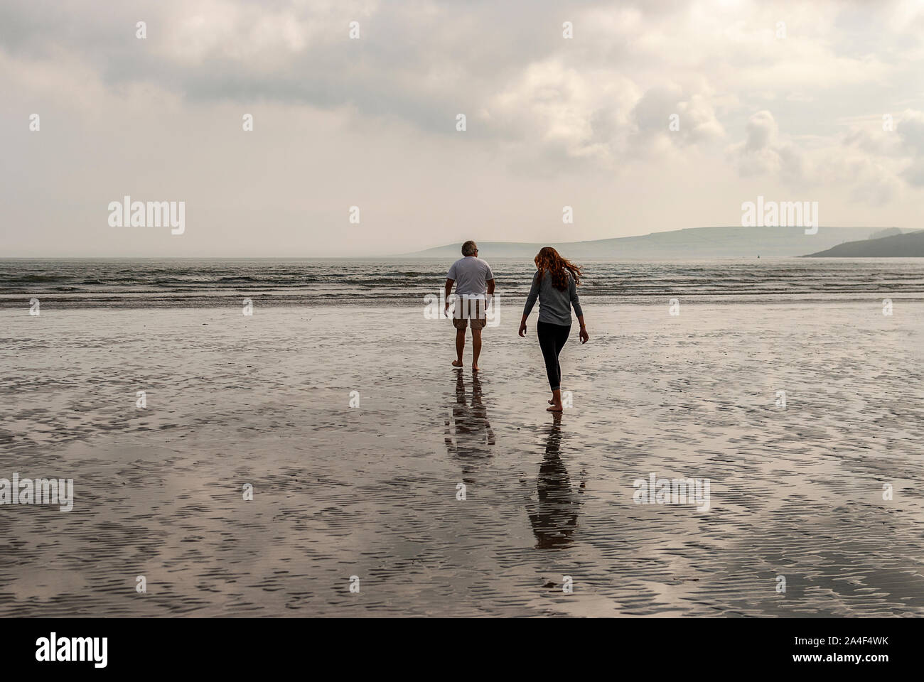 Couple walking on sandy beach leaving footprints in the sand. One father and his daughter enjoying the day. Cloudy day. Stock Photo
