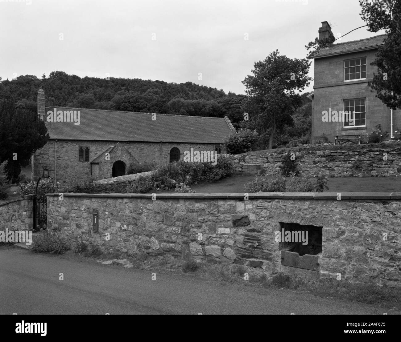 View N of St Mael and St Sulien's church & former vicarage (Ty Cerrig) in Cwm, Denbighshire, Wales, UK. Animal drinking trough set into garden wall. Stock Photo
