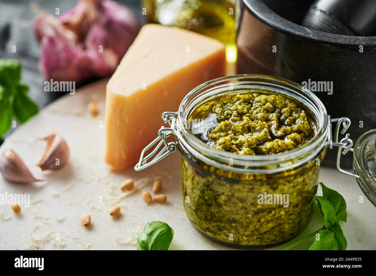 Pesto sauce or pesto genovese in a glass jar with pine nuts, parmesan, basil, oil and garlic on white marble cutting board. Copy space. Stock Photo