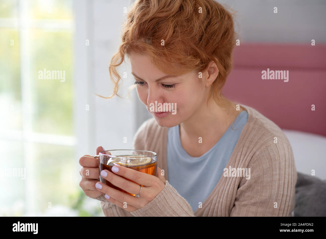 Curly sick woman feeling good while drinking hot tea Stock Photo