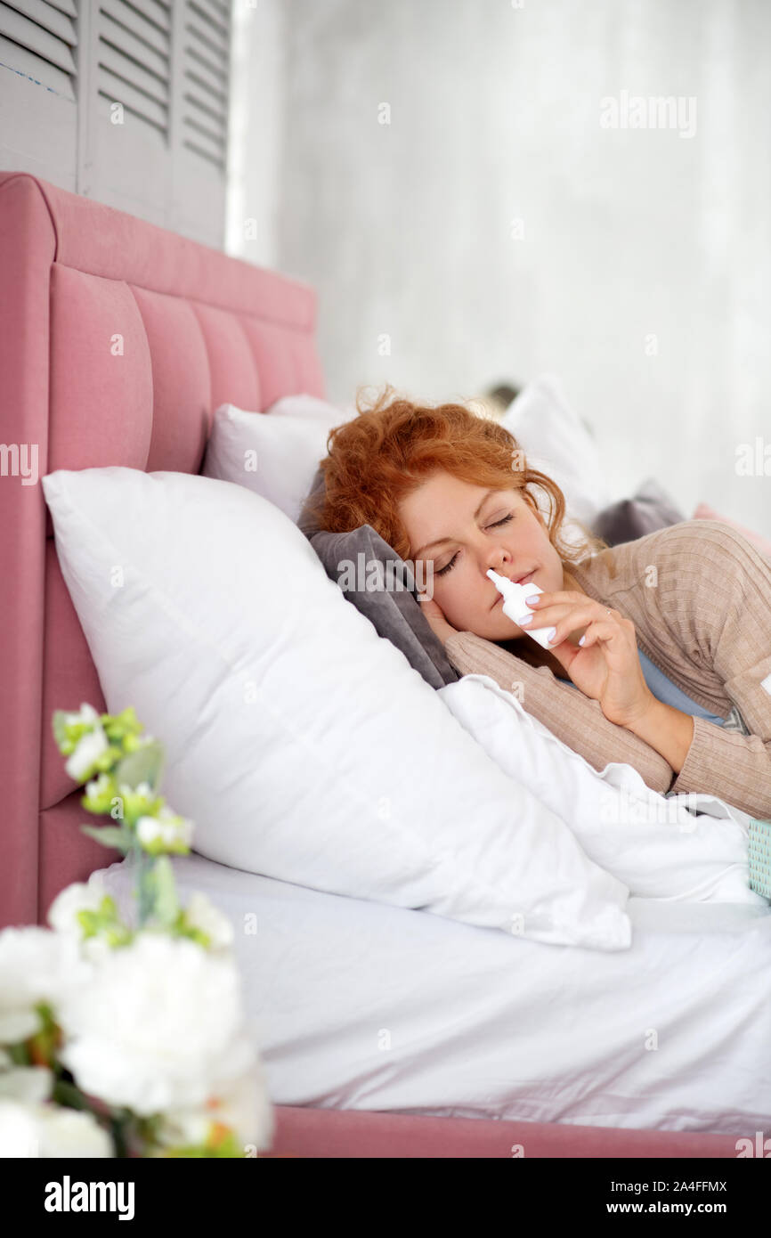 Sleepy sick woman using nasal spray while having stuffy nose Stock