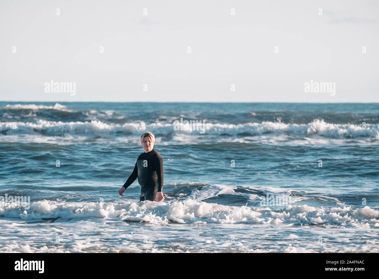 Tween boy wearing a wetsuit standing in the water at the beach Stock