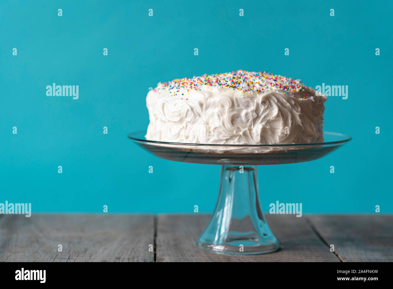 Birthday cake with white icing and sprinkles against blue background ...