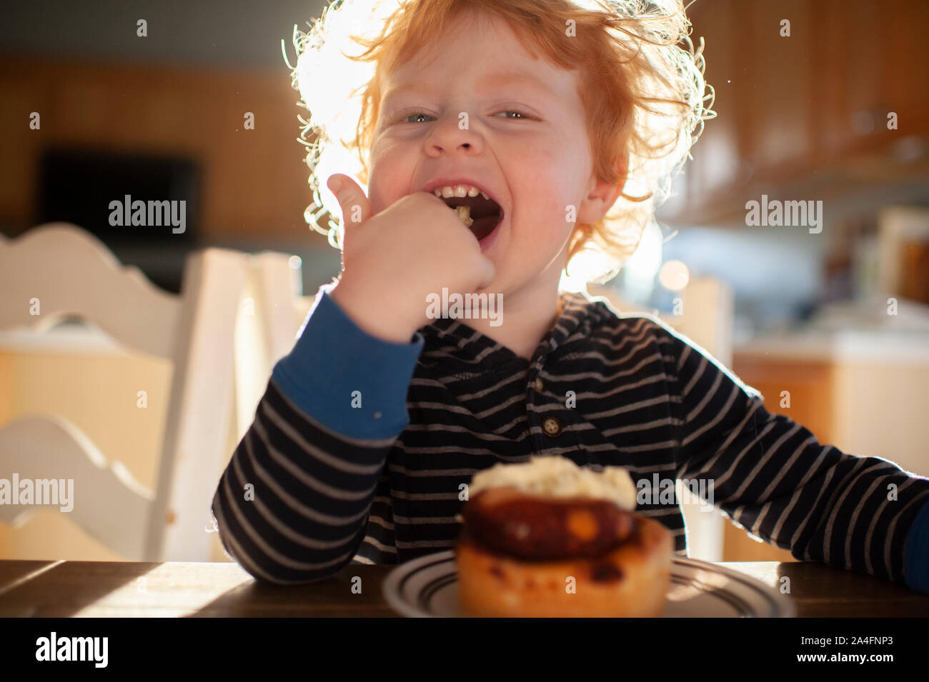 Toddler boy sitting at table licking frosting from finger at breakfast Stock Photo