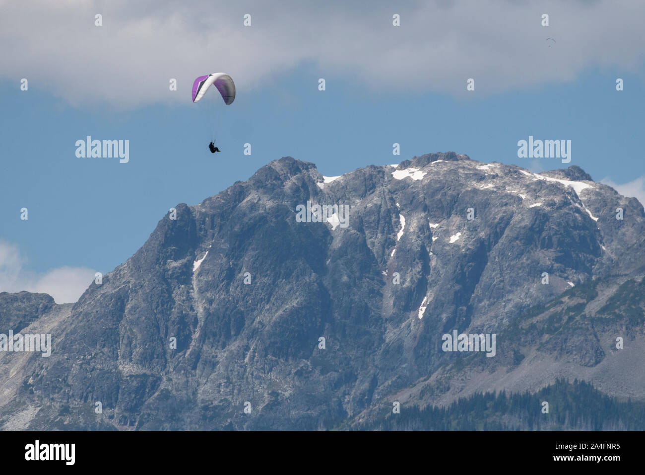 Paragliders fly high above snow covered mountains on a sunny day. Stock Photo