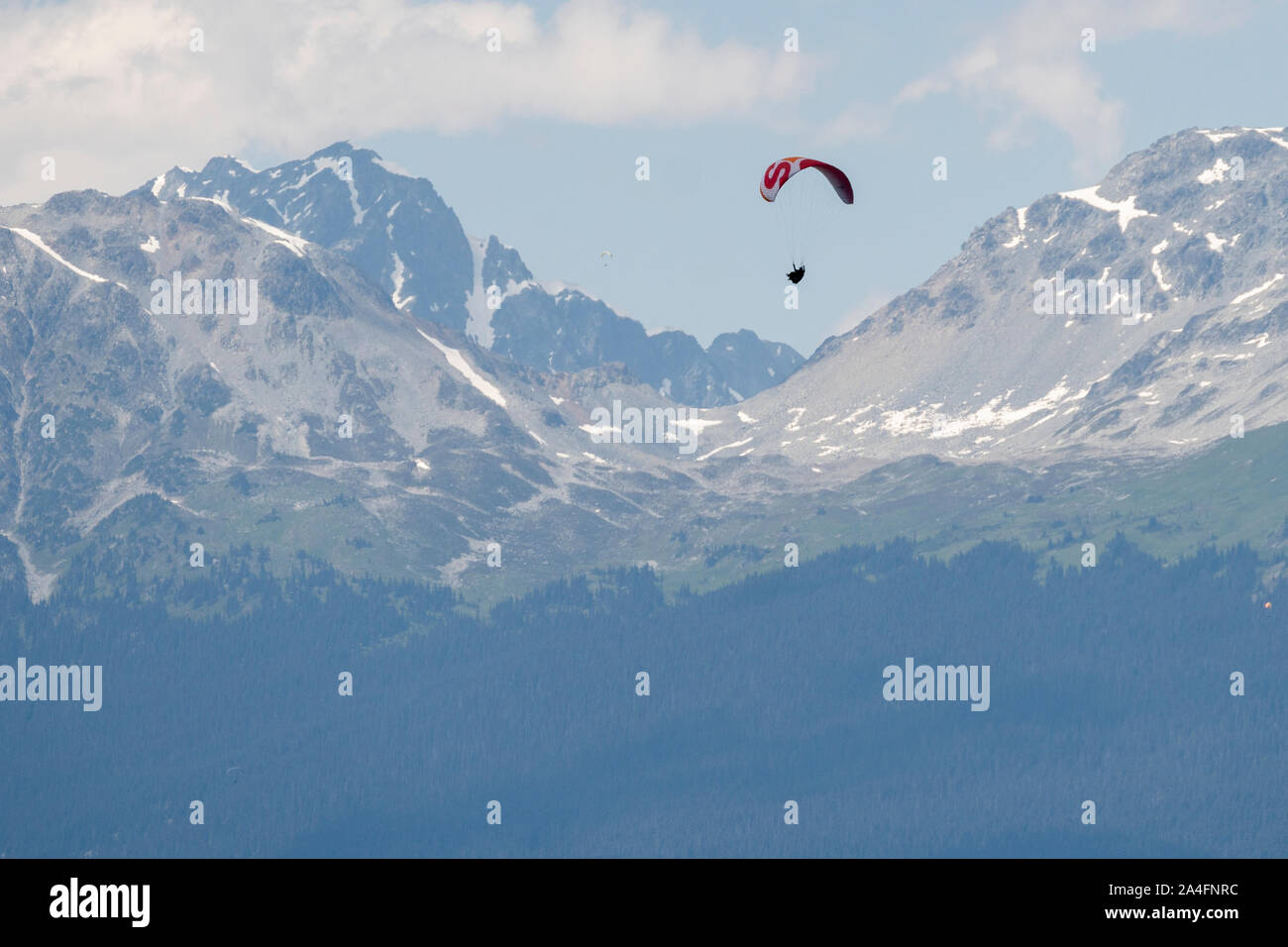 Paragliders fly high above snow covered mountains on a sunny day. Stock Photo