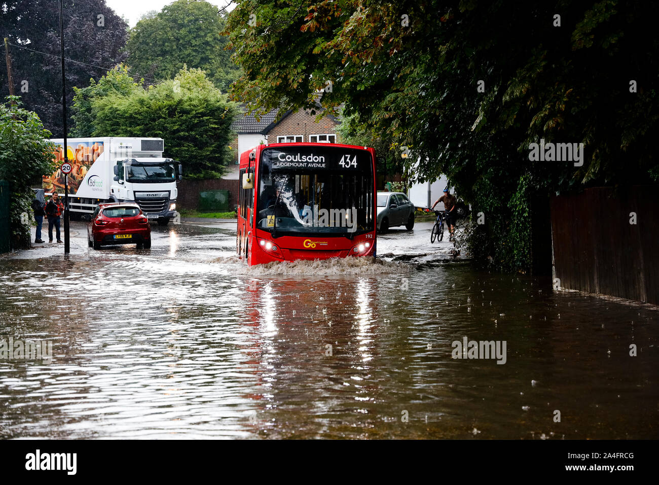London, UK. A red bus splashes through flood water in Kenley, south London, after torrential rain caused the road to flood in under half an hour. Stock Photo
