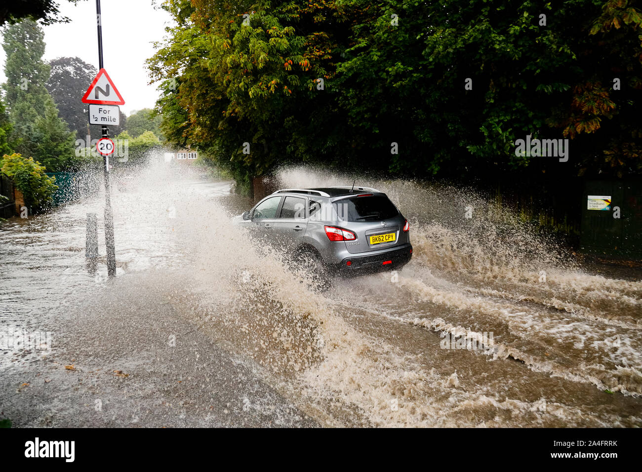 London, UK. A Nissan Qashqai enters flood water at high speed in Kenley, south London, where torrential rain caused the road to flood in under half an Stock Photo
