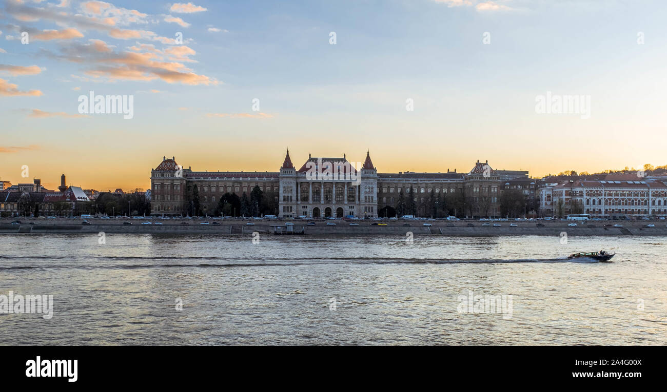 A boat driving by the Budapest University of Technology and Economics during sunset. Stock Photo