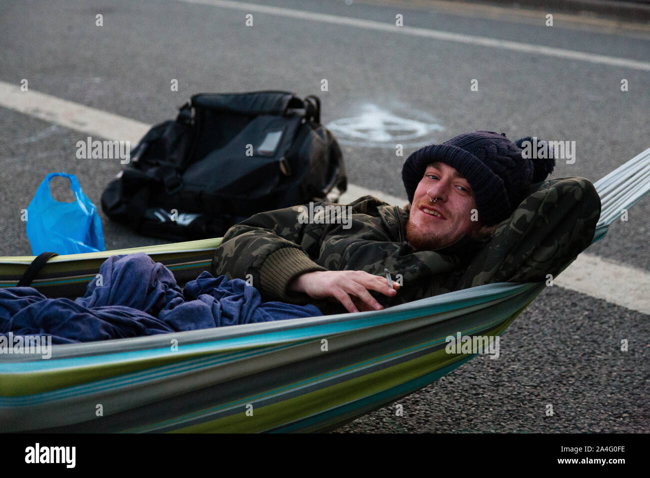 London, UK. An Extinction Rebellion protester smokes a cigarette in his hammock on Waterloo Bridge in the early morning. Stock Photo