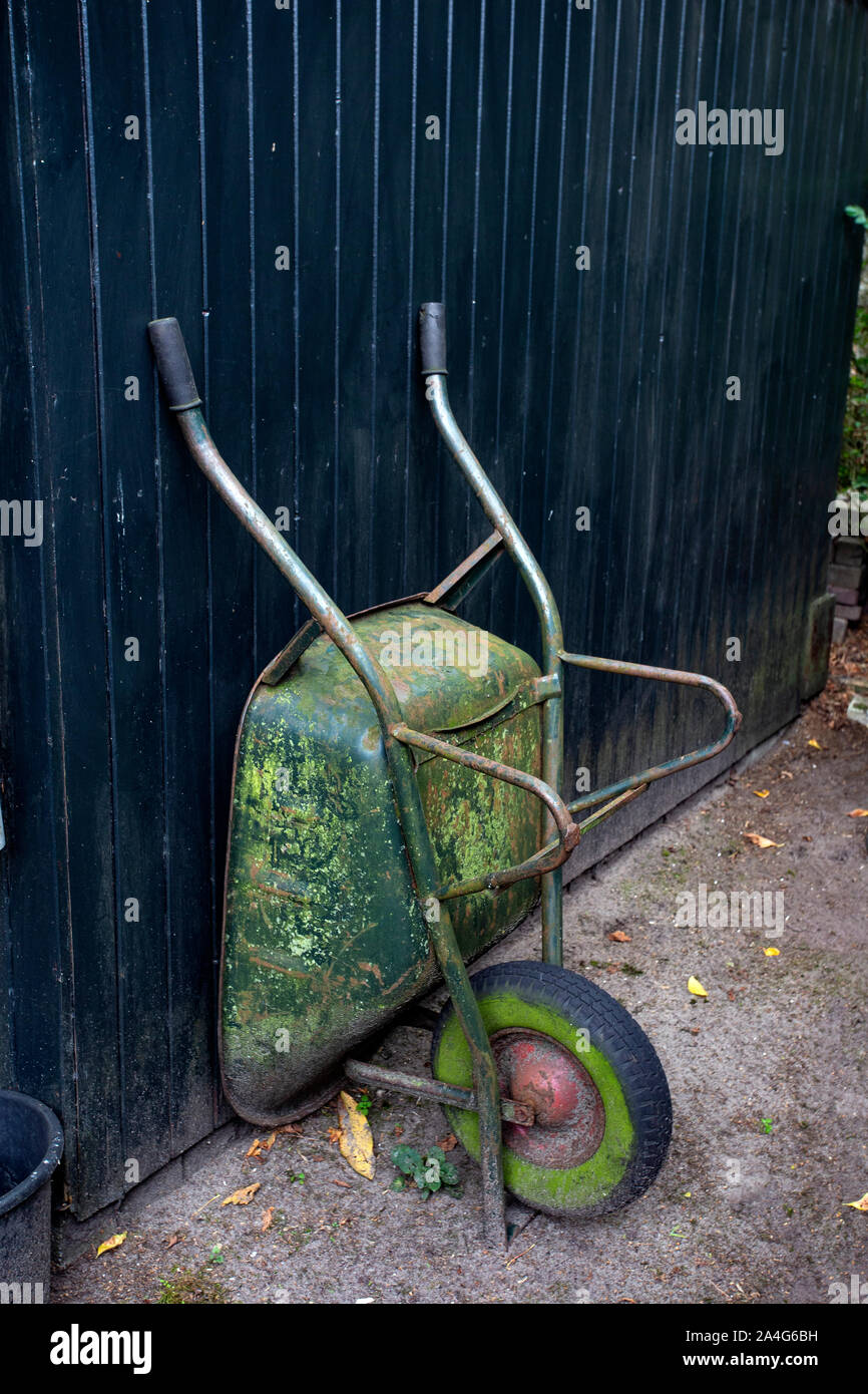 Old and rusty wheelbarrows rest against wall of farm barn Stock Photo