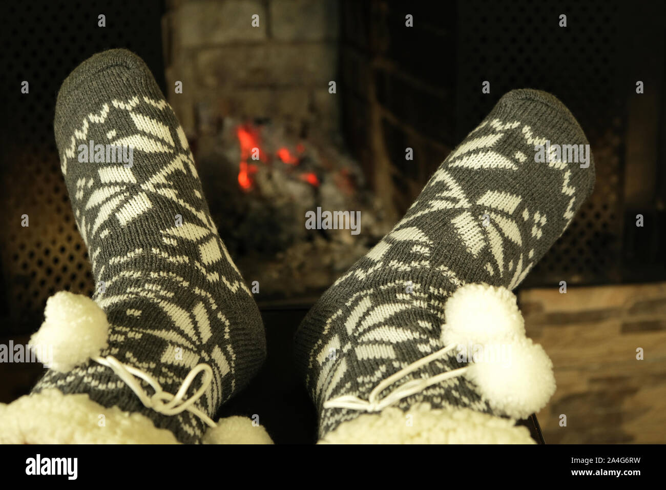 feet in woolen winter warm socks with white ornament and  pom poms near fireplace in winter evening, concept of relaxing cozy New Year celebration Stock Photo