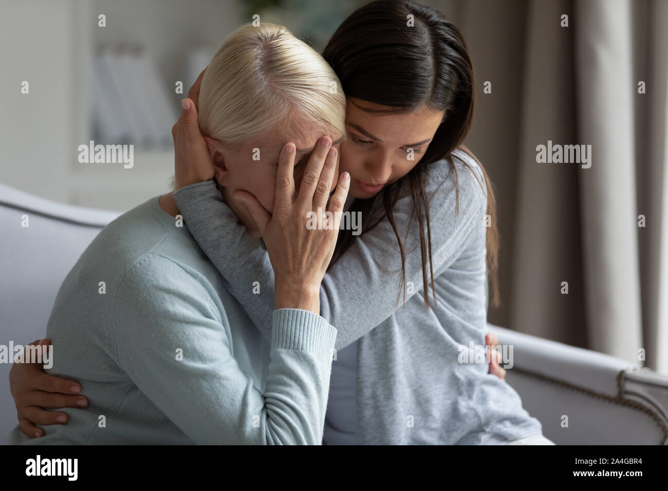Empathic young lady embracing soothing crying depressed elder mommy. Stock Photo