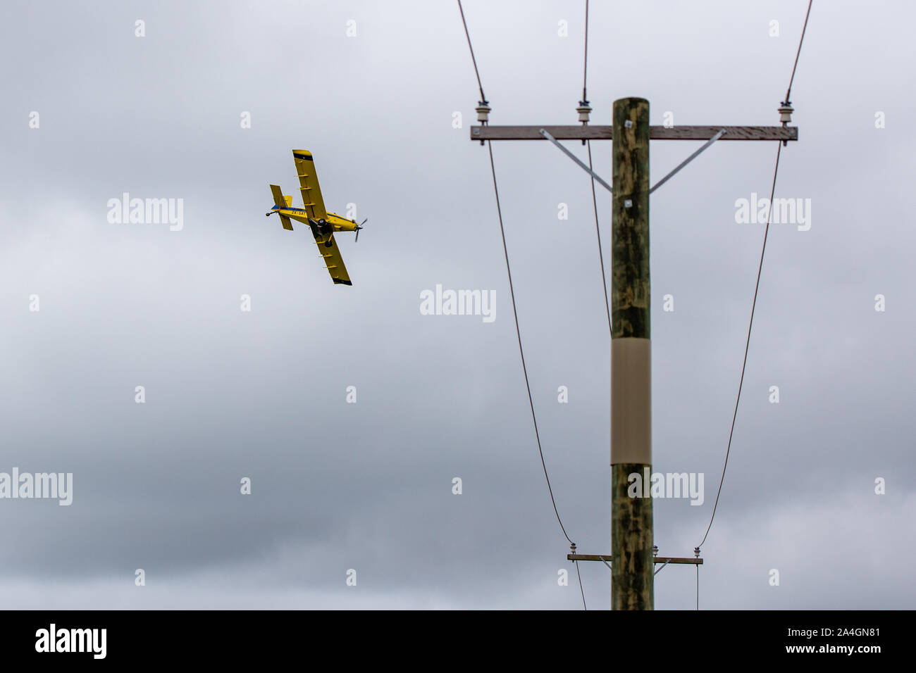 Sheffield, Canterbury, New Zealand, October 14 2019: A yellow crop duster, or top dressing plane, passes low over power lines as it spreads fertiliser Stock Photo