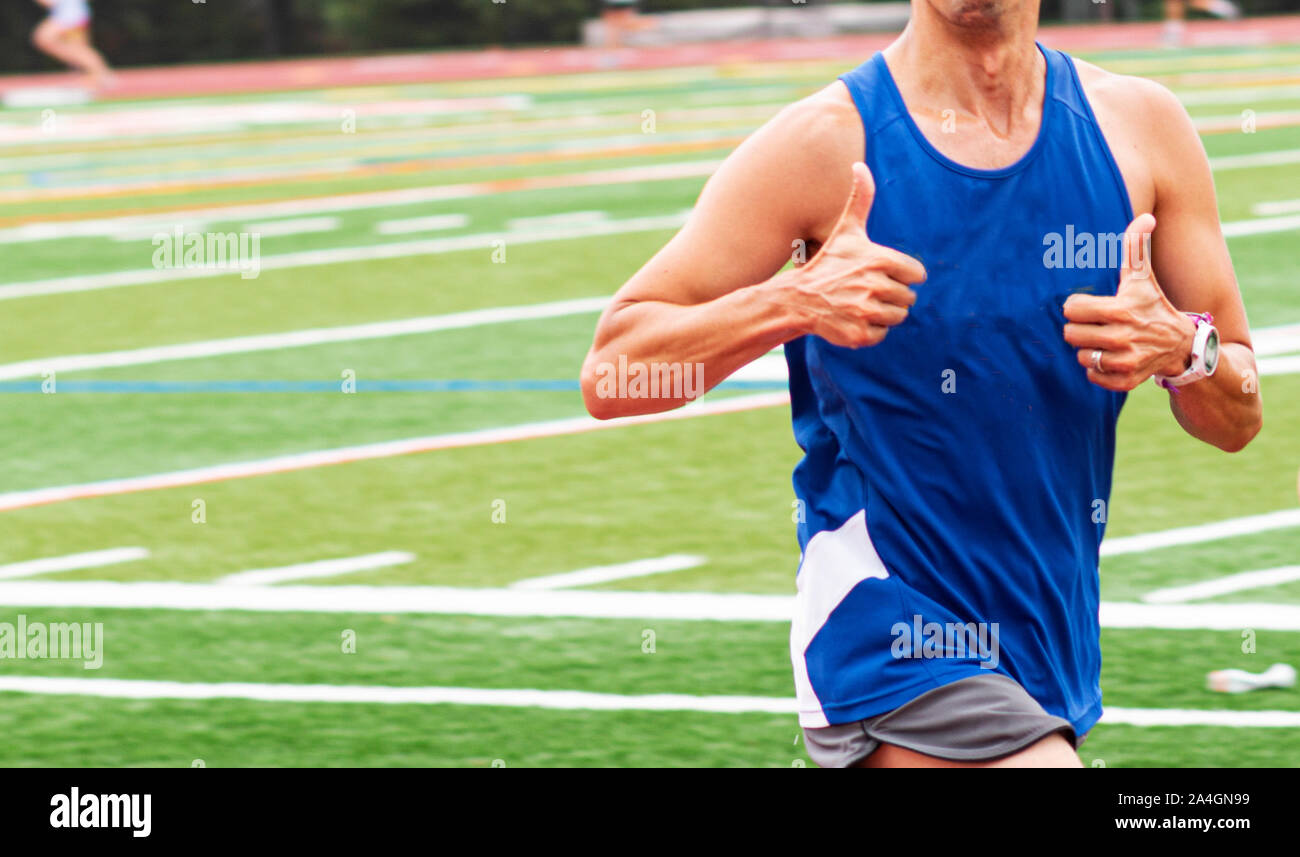 A runner in a blue tank top gives the photographer two thumbs up while ...