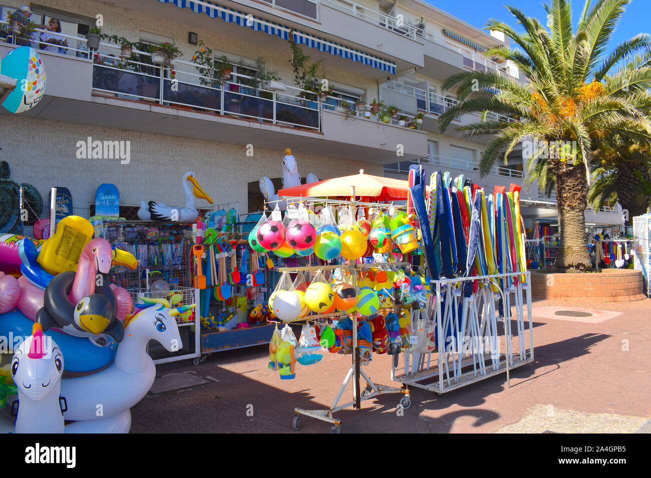 Well stocked shop on the promenade in south of France selling pool and beach floats and inflatables, beach games, beach sets and toys. Tall palm tree. Stock Photo