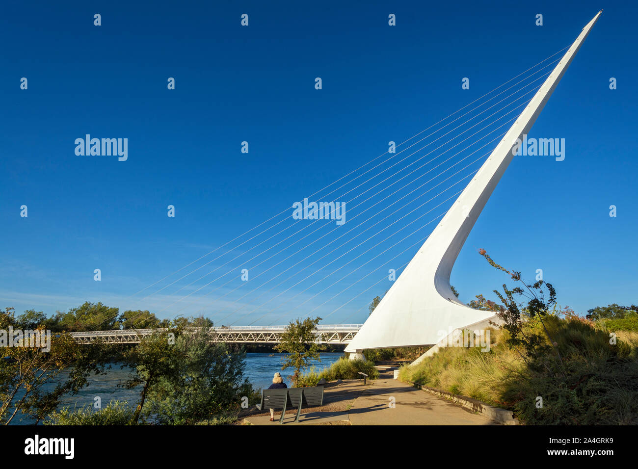 California, Redding, Sundial Bridge at Turtle Bay Exploration Park, spans Sacramento River, woman stting on bench Stock Photo