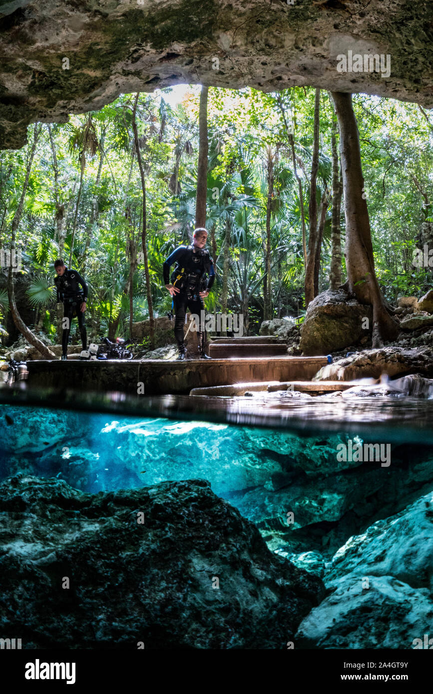 Two scuba divers exit Tajma Ha Cenote into the Jungle. Stock Photo