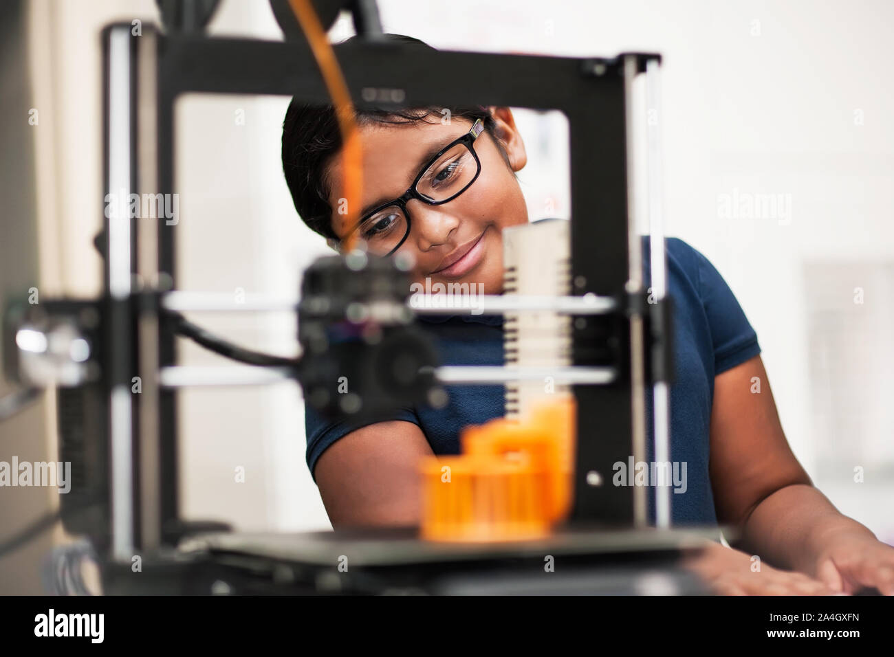 A smart little girl admiring her 3D printed model from behind the 3D printer. Stock Photo