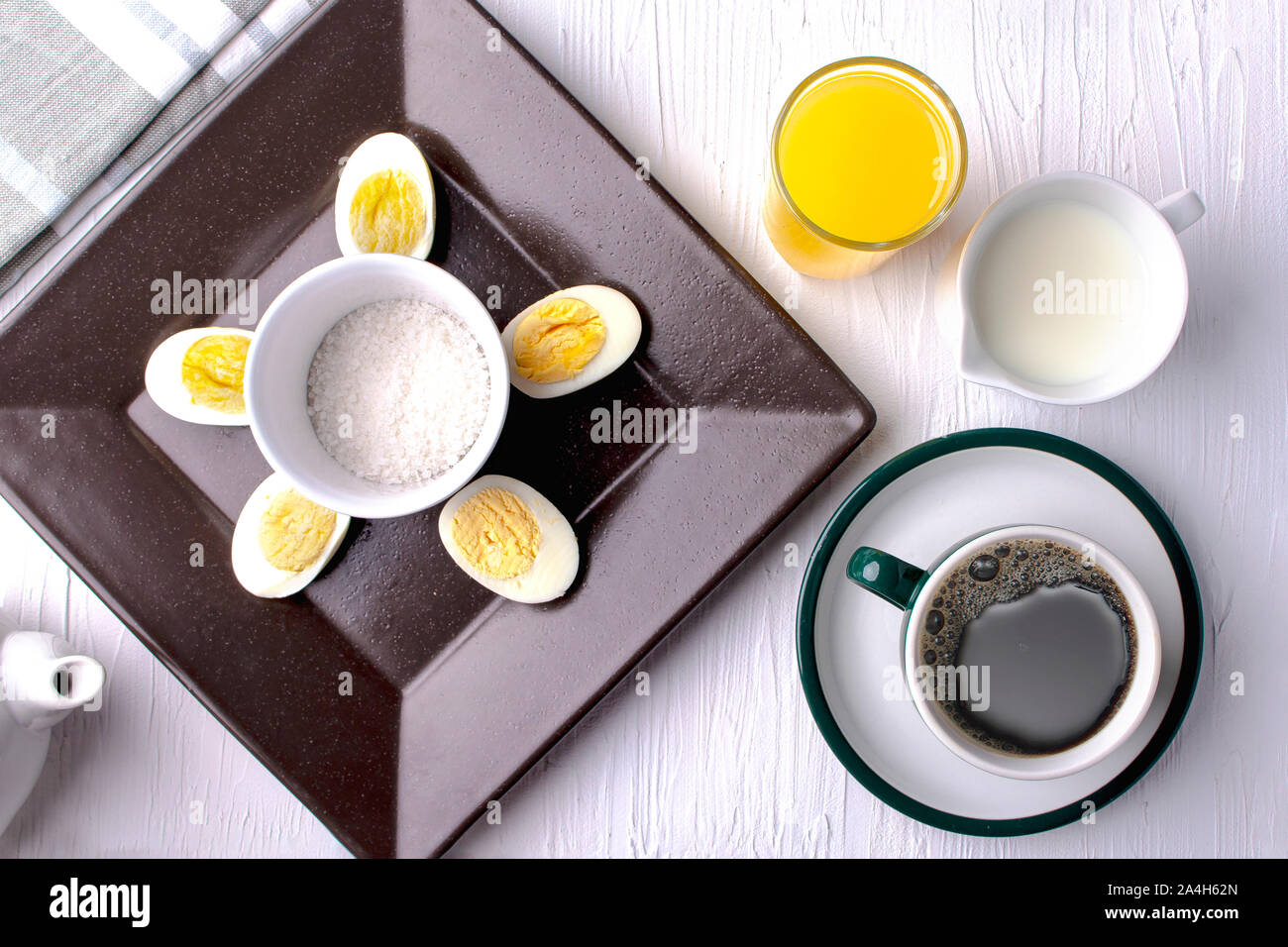 Boiled eggs on a brown plate with coffee, cream and orange juice and salt Stock Photo