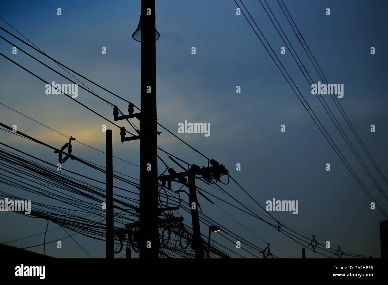 electrical power and telecommunication lines silhouette. blue hour after sunset. irregular and chaotic arrangement pattern. unordered poor design of t Stock Photo