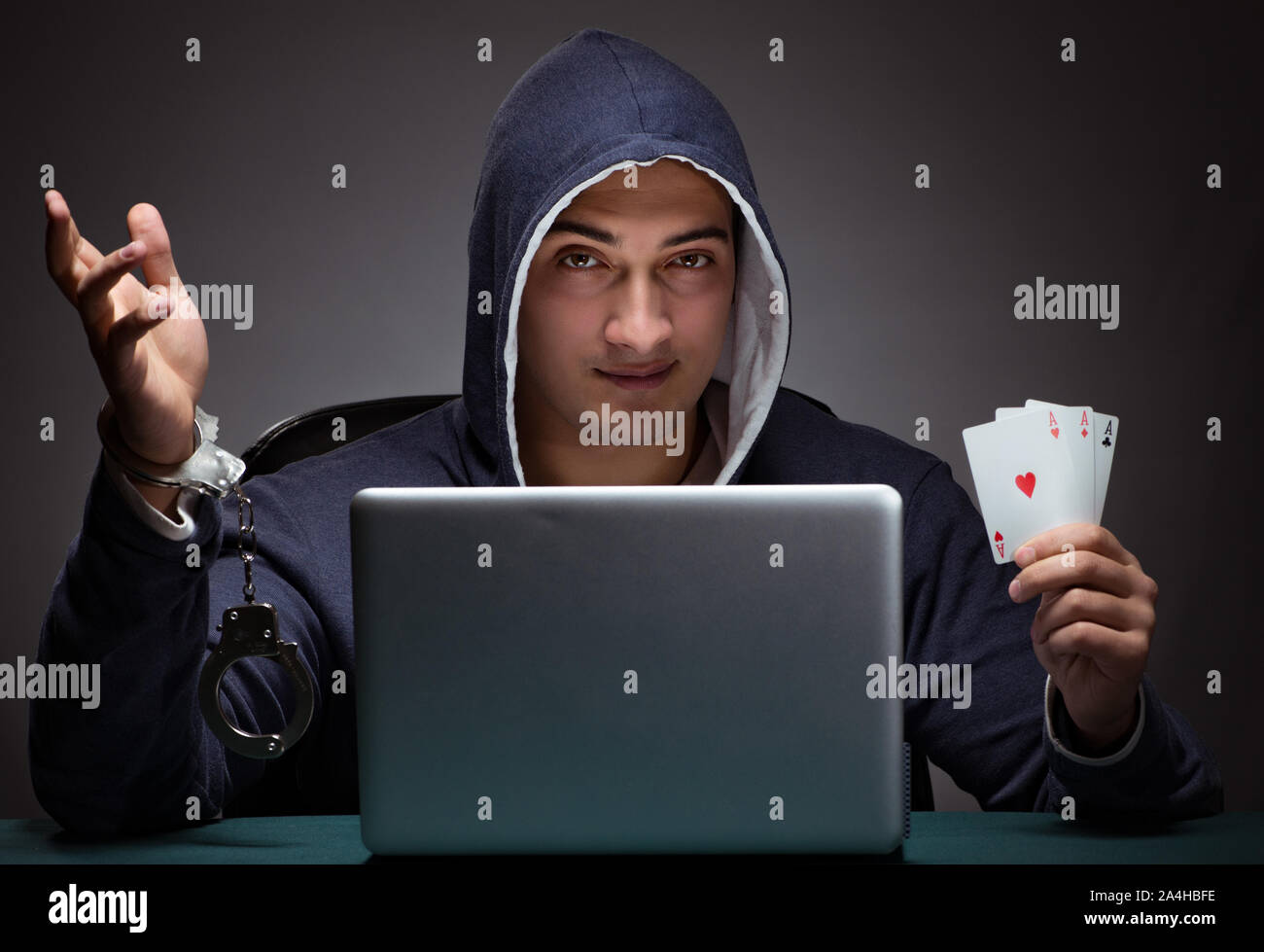 Young man in handcuffs wearing a hoodie sitting in front of a laptop computer gambling Stock Photo