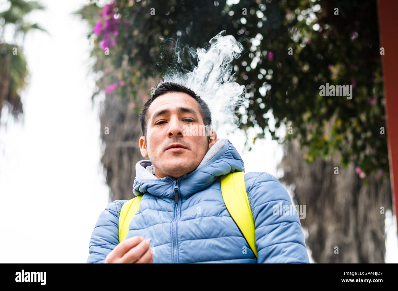 A man with a backpack smoking and smoke coming out of his mouth Stock