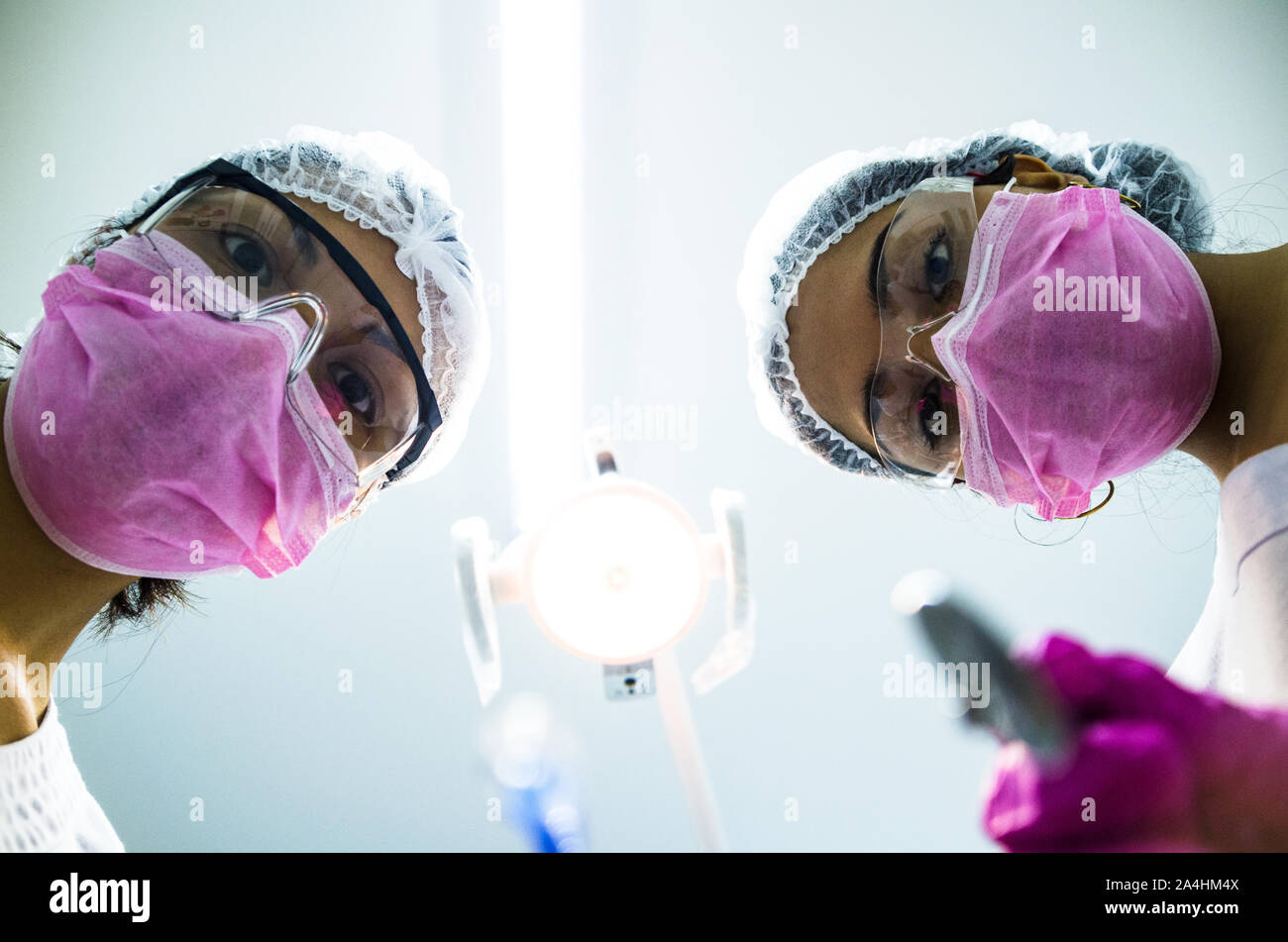 Bottom view of two women dentists in surgical mask holding tools and looking at camera. Patient point of view to dentist. Stock Photo