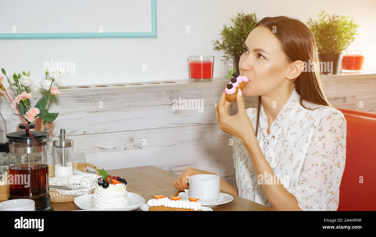 happy girl in summer dress eats delicious cake decorated with cream and berries at table in modern sweet shop Stock Photo
