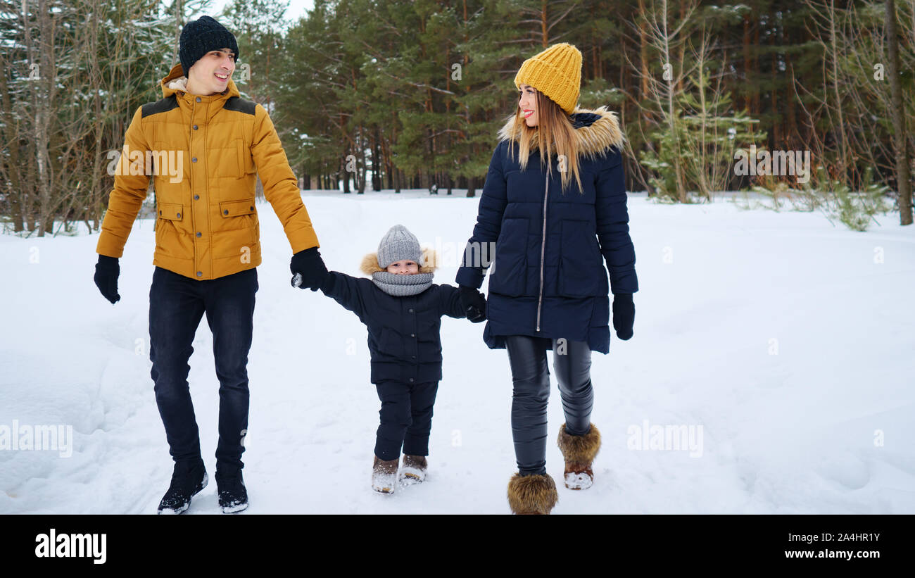 Portrait of happy family walk in winter day. Mom and dad are holding hands their little son in winter park, copy space. Family lovely moments. Stock Photo