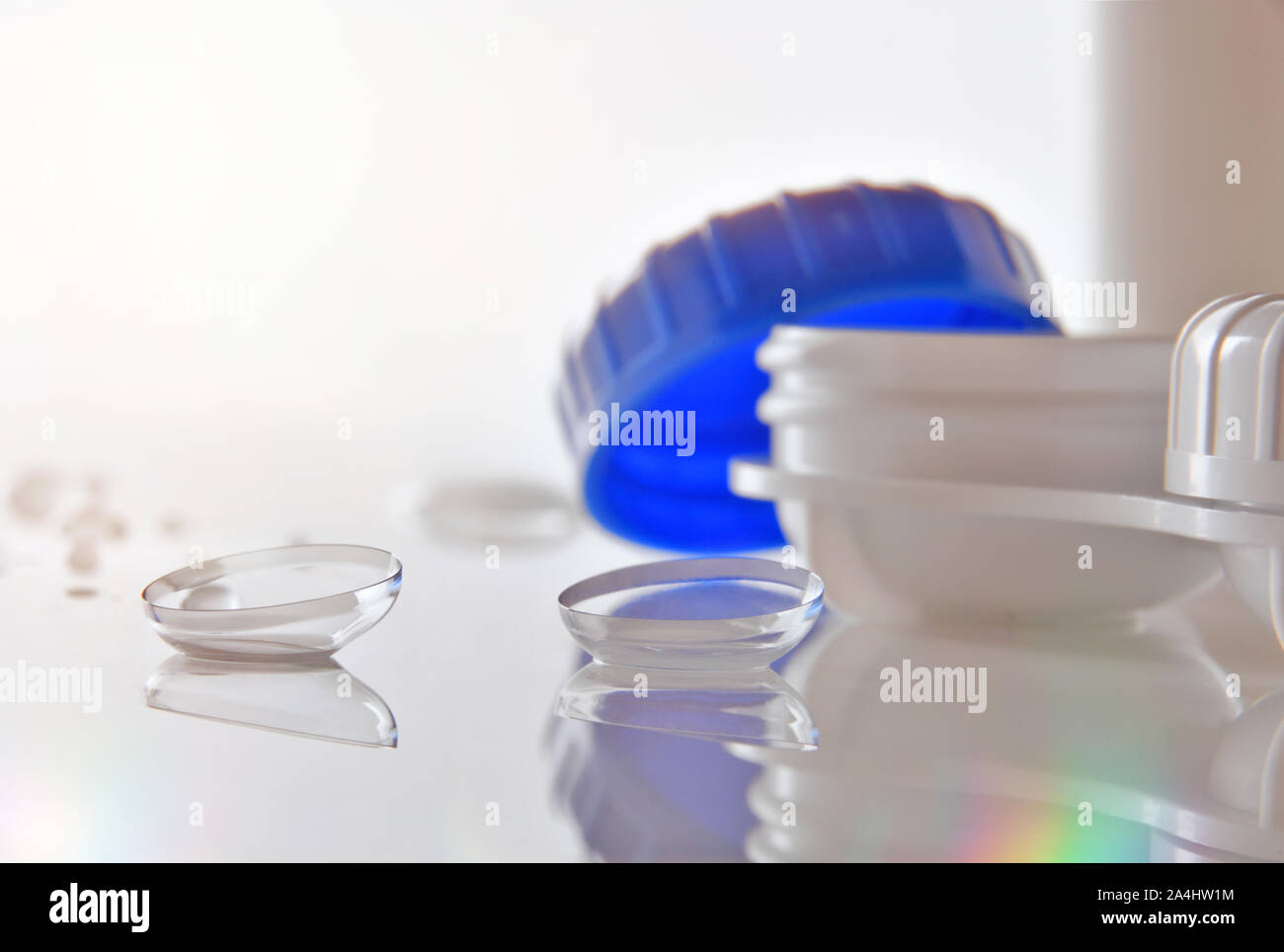 Contact lenses reflected on glass table with lens case and water drops. Horizontal composition. Front view. Stock Photo