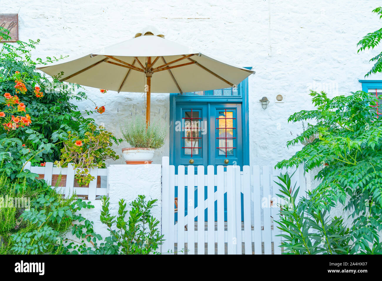 Blue front door under shade umbrella with quaint white fence, gate and garden photographed from street. Stock Photo