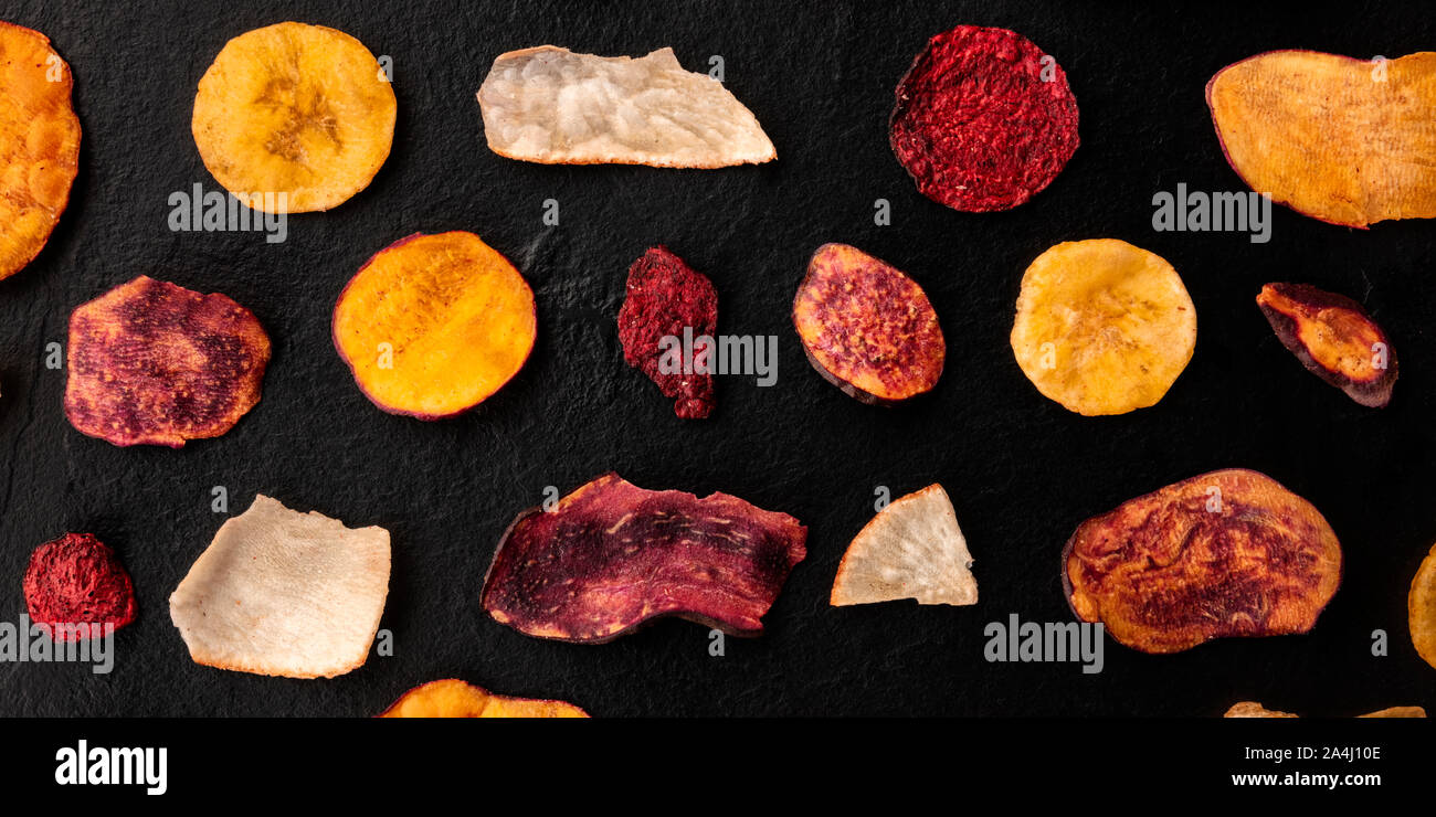 A panorama of dry fruit and vegetable chips, shot from the top. Healthy vegan snack, an organic food flat lay pattern on a black background Stock Photo