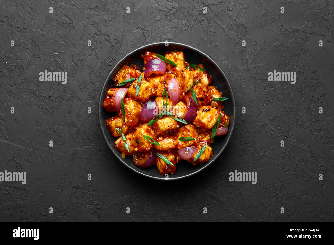 Schezwan Paneer in black bowl at dark slate background. Schezwan Paneer is indo-chinese cuisine dish with deep fried Paneer cheese, onion and Schezwan Stock Photo