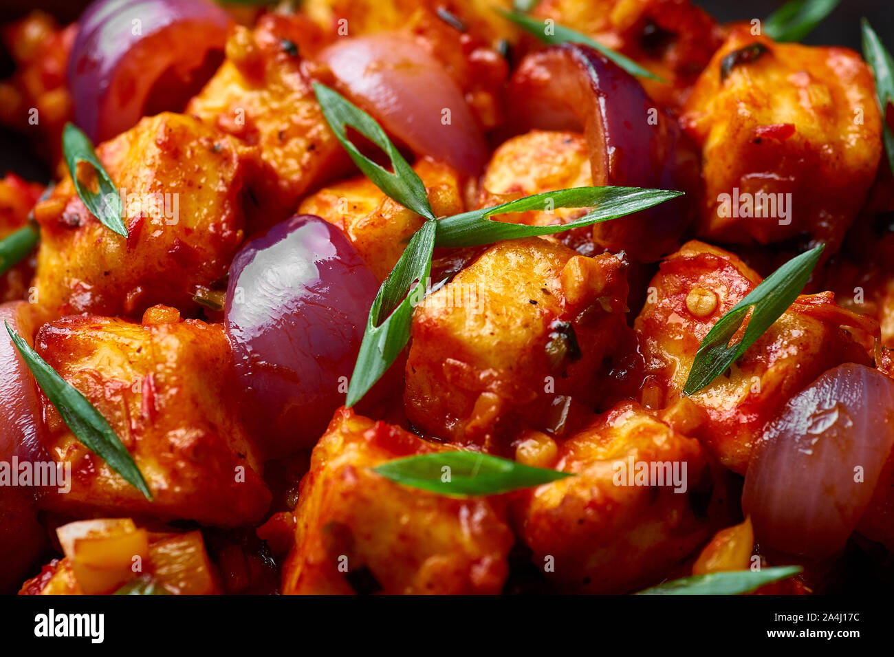 Schezwan Paneer in black bowl at dark slate background. Schezwan Paneer is indo-chinese cuisine dish with deep fried Paneer cheese, onion and Schezwan Stock Photo