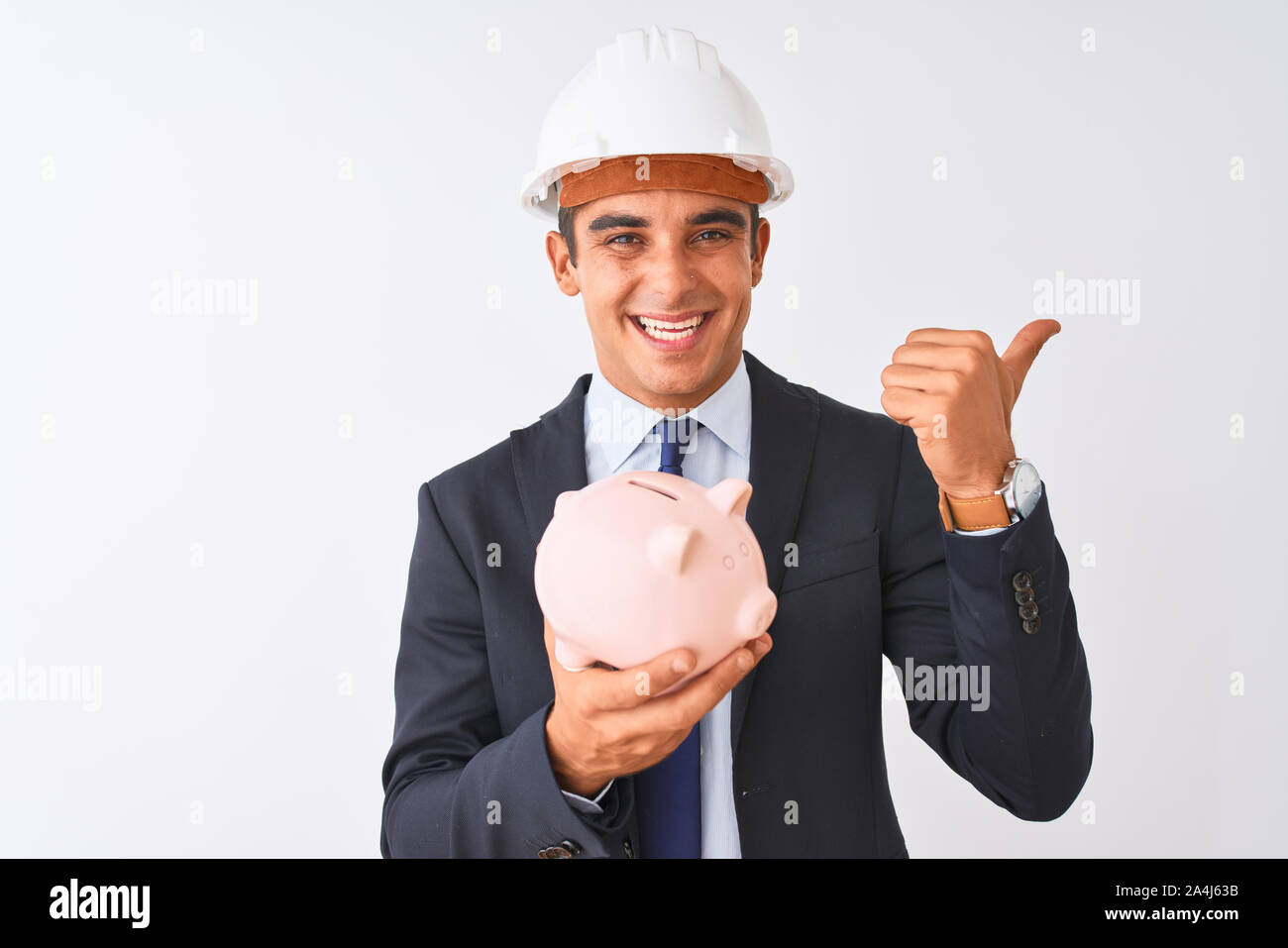 Handsome architect man wearing helmet holding piggy bank over isolated ...