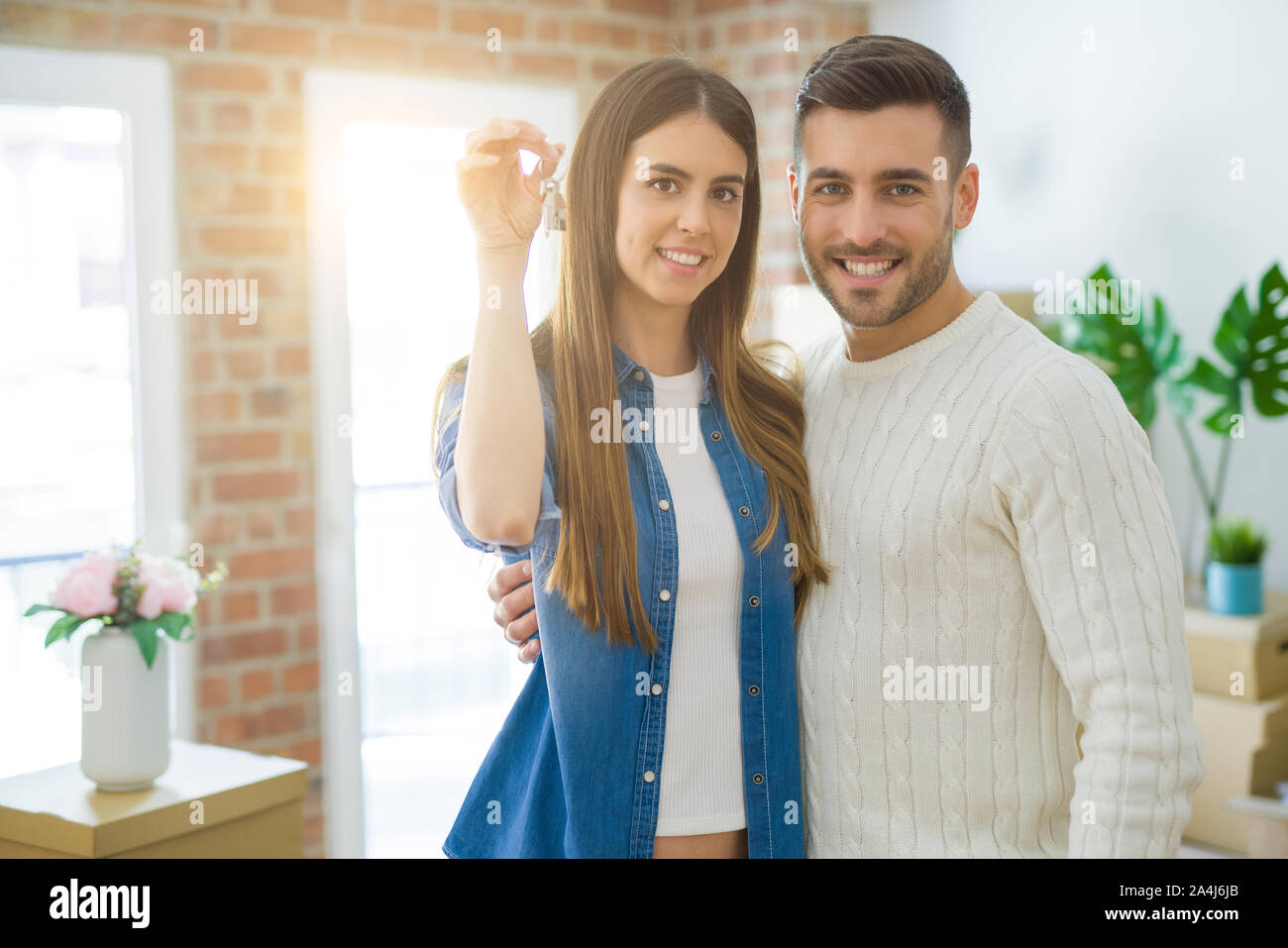 Young couple moving to a new home, hugging in love showing keys of new ...