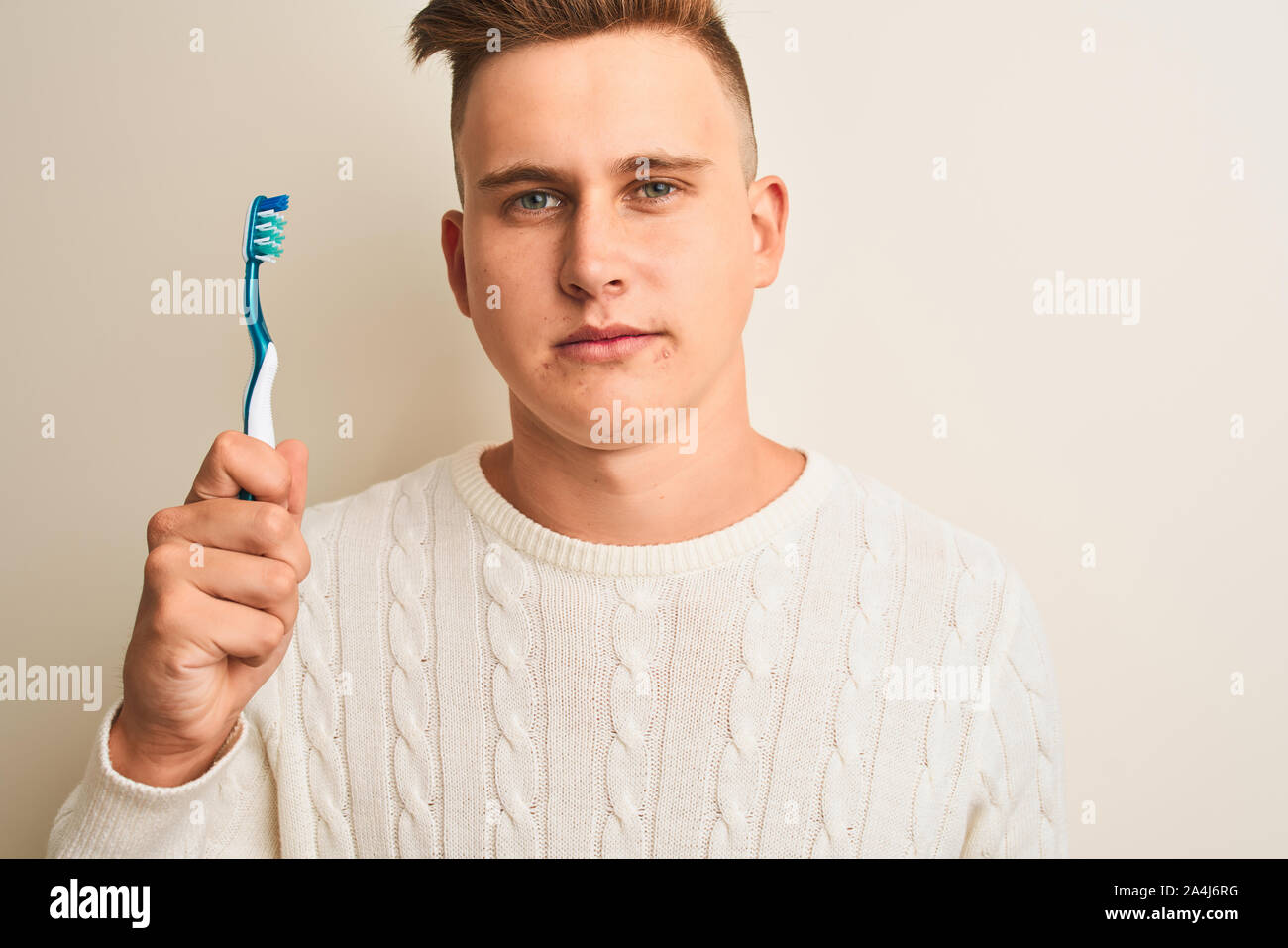 Young handsome man holding tooth brush standing over isolated white background with a confident expression on smart face thinking serious Stock Photo