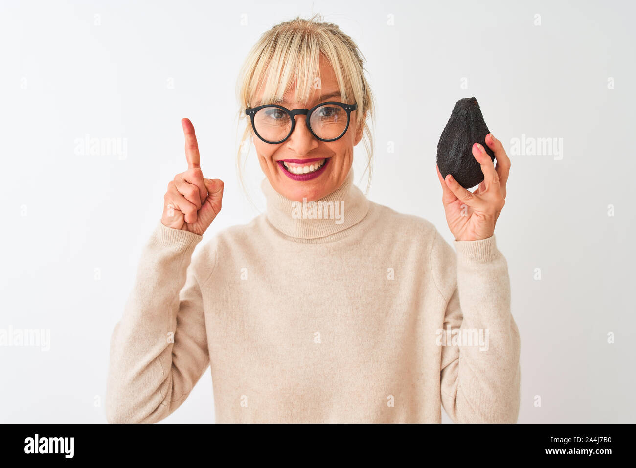 Middle age woman wearing glasses holding avocado over isolated white background surprised with an idea or question pointing finger with happy face, nu Stock Photo