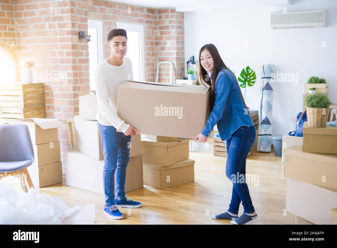 Beautiful young asian couple looking happy, holding a big cardboard box ...