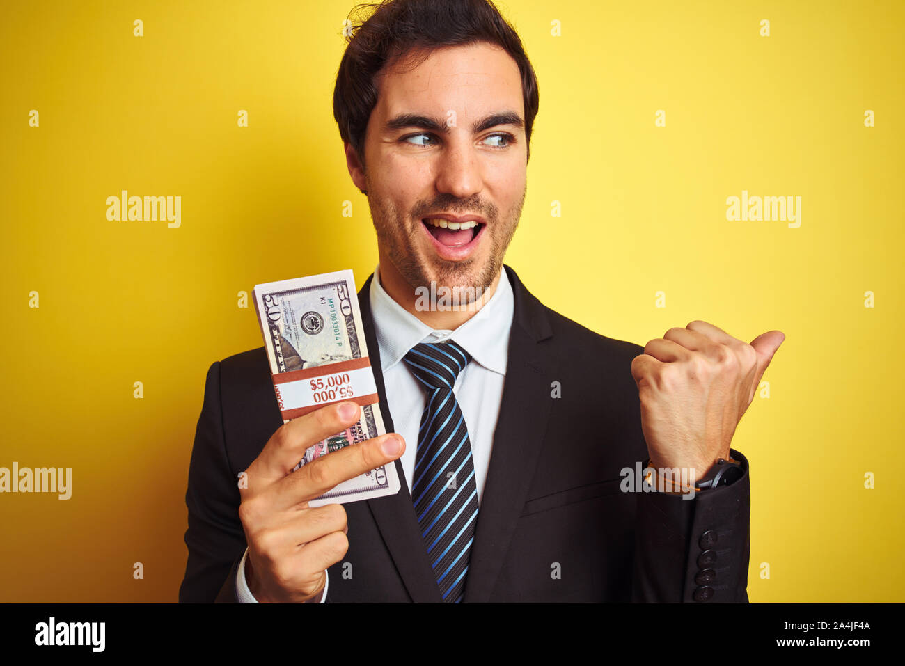 Young handsome businessman wearing suit holding dollars over isolated ...
