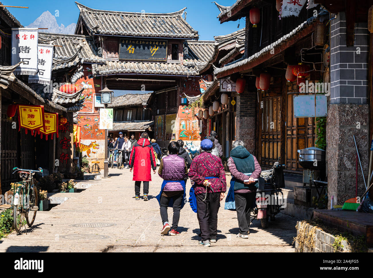 Baisha, China - February 11 2019: Local people walk toward the traditional Bai Sha Naxi village entrance gate near Lijiang in Yunnan province Stock Photo