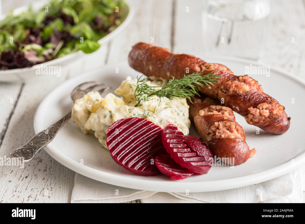 Isterband sausage with dill stewed potatoes and pickled beetroots, traditional Swedish food. On a white wooden table, with a green salad in the backgr Stock Photo