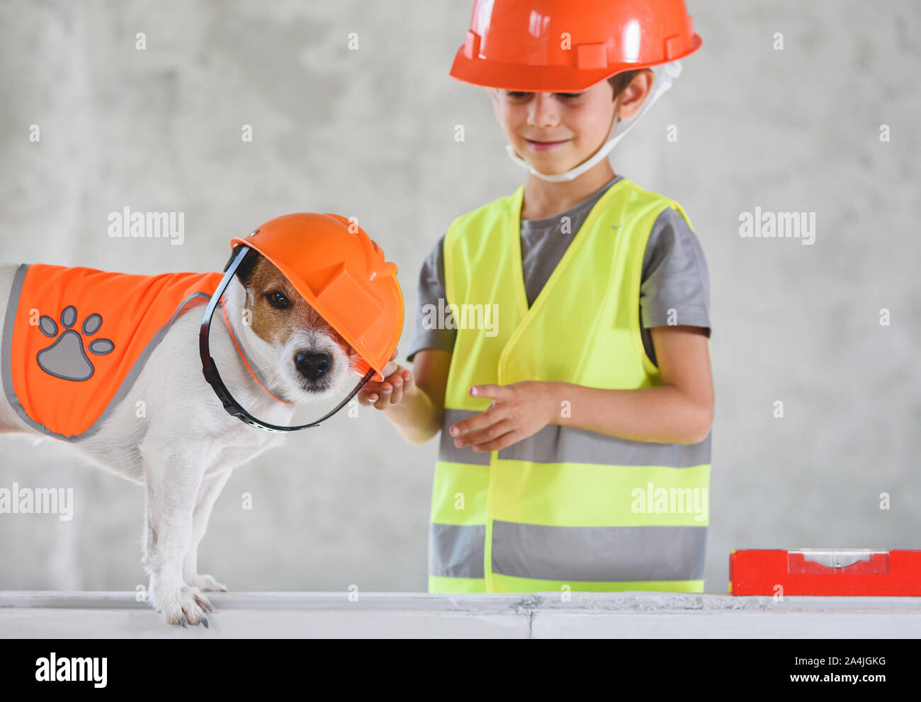 Funny dog wearing crookedly hardhat at construction site and kid in protective clothes Stock Photo